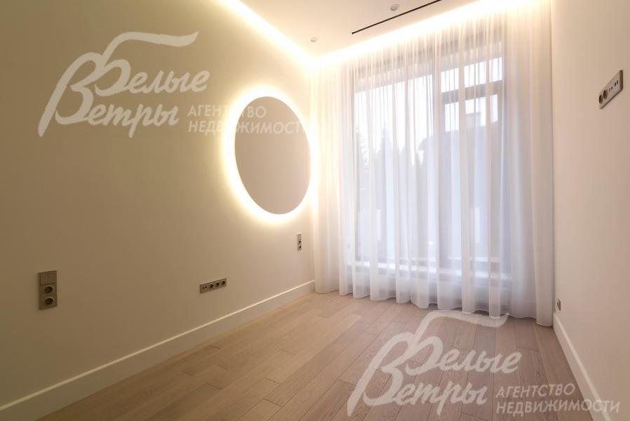 Одна из спален дома с многоуровневой подсветкой, большим окном с изящными шторами