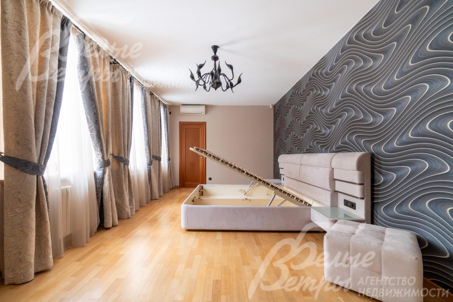 Мастер-спальня на втором этаже: кровать расположена напротив трёх больших окон, декорированных элегантными шторами