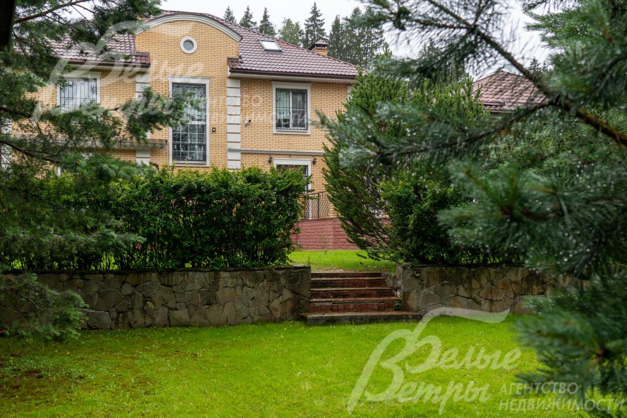 На верхний уровень участка с домом ведут ступени, уровни разграничены подпорной стенкой, отделанной диким камнем