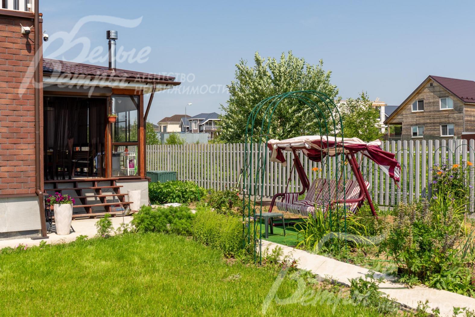 На участке стоят качели, арка для розария, есть теплица