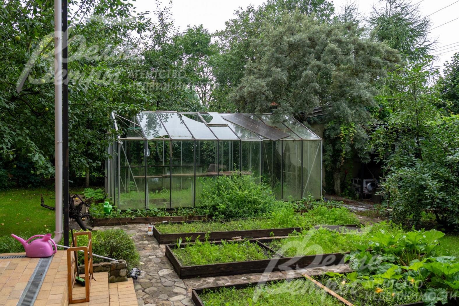 На участке организована садовая зона с высокими грядками и теплицей