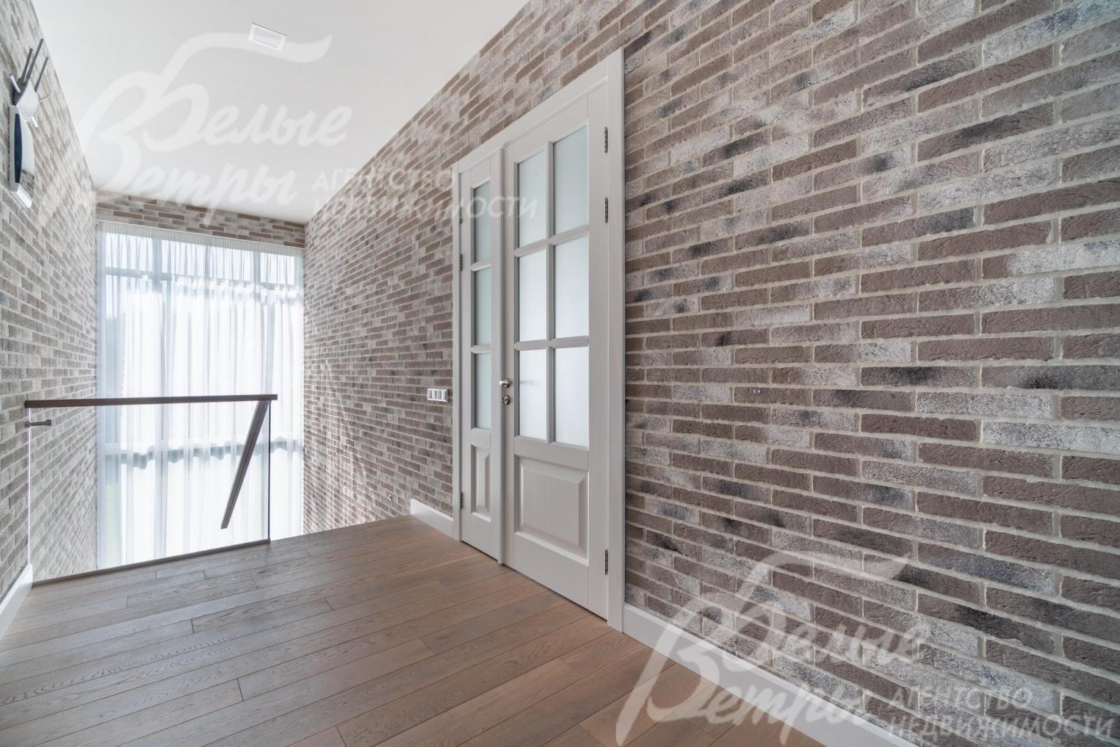 Холл второго этажа с декоративной отделкой стен "под кирпич" и белыми дверями из массива дуба