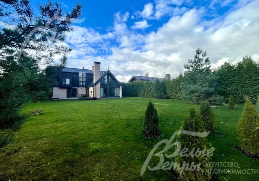 На участке газон, по периметру высажены молодые деревья: туи, сосны