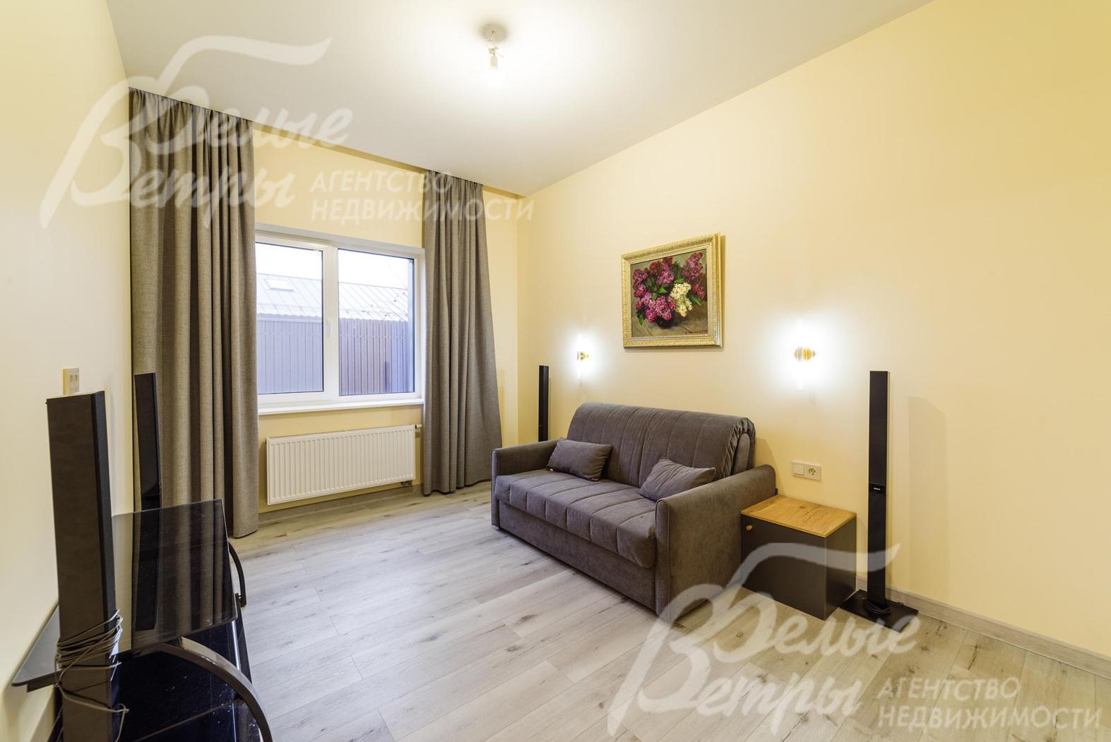 Одна из спален дома с диваном и тумбой под ТВ. Интерьер выдержан в спокойной нейтральной гамме