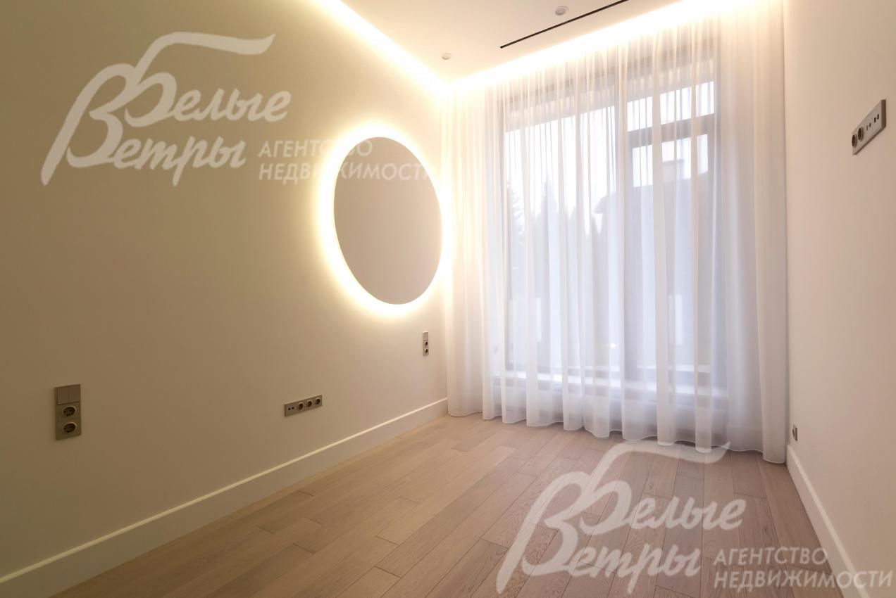 Одна из спален дома с многоуровневой подсветкой, большим окном с изящными шторами