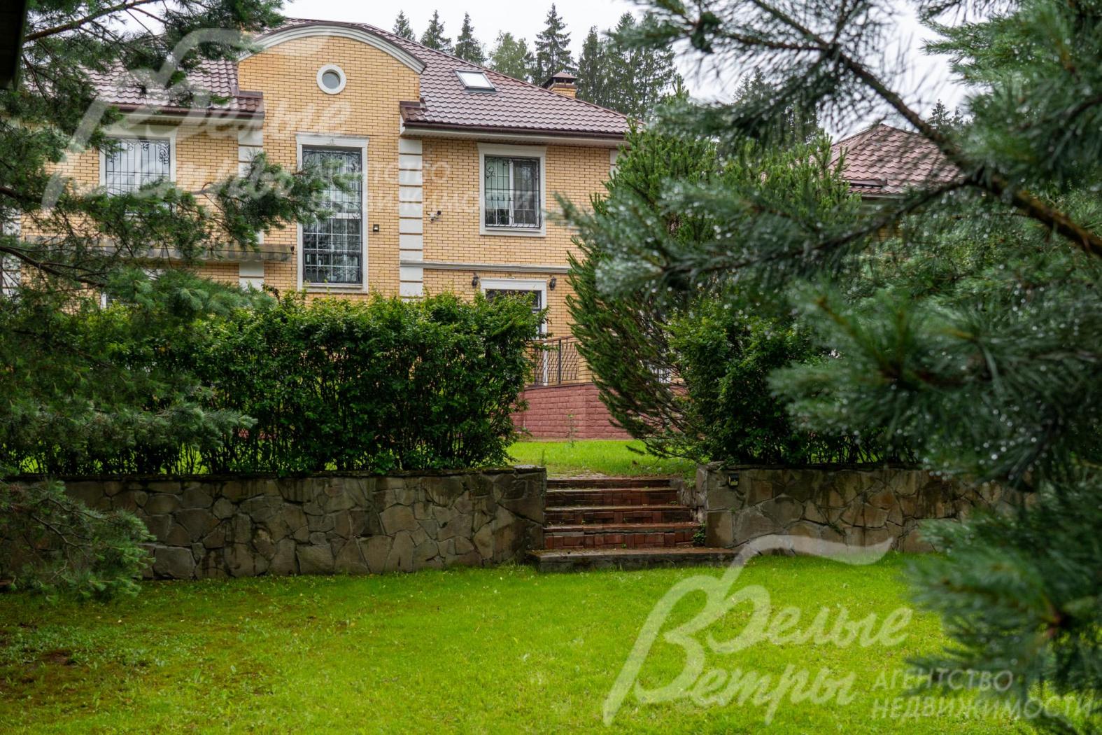 На верхний уровень участка с домом ведут ступени, уровни разграничены подпорной стенкой, отделанной диким камнем